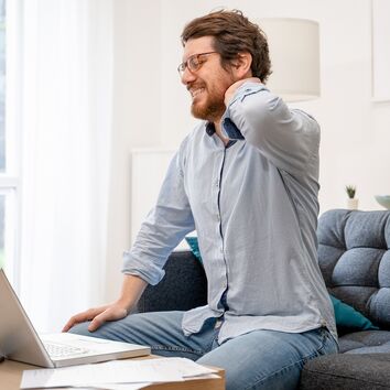 Mann mit Nackenscmerzen fasst sich an den oberen Rücken